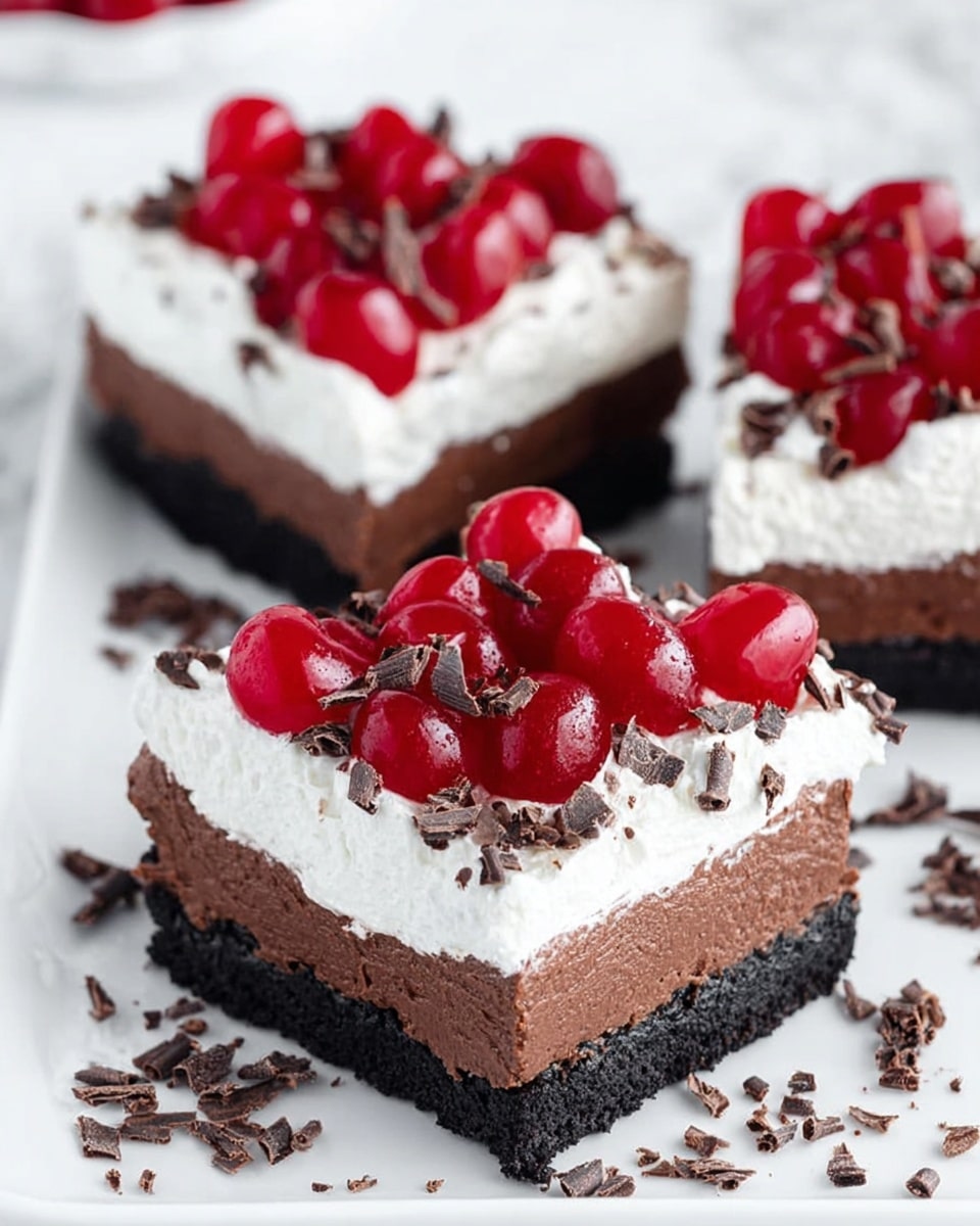 The image shows square chocolate cakes on a white plate placed on a white marbled texture. Each cake has three visible layers: a dark black crust at the bottom, a thick smooth dark brown chocolate layer in the middle, and a fluffy white whipped cream layer on top. Bright red cherries cover the center of the whipped cream, surrounded by small dark chocolate shavings scattered on the cream and around the plate. Photo taken with an iphone --ar 4:5 --v 7