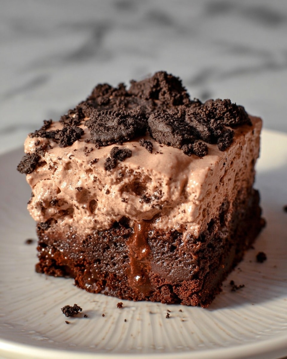 The image shows a single square piece of chocolate dessert on a white plate with a subtle pattern. The dessert has two main layers: the bottom layer is a dense, moist dark chocolate cake with a textured surface and some shiny, gooey spots indicating melted chocolate inside. The top layer is a thick, creamy, light brown chocolate mousse with a smooth but slightly uneven texture. Scattered over the top and partly on the sides are crumbly, dark chocolate cookie pieces, adding contrast and crunch. The background is a white marbled surface. photo taken with an iphone --ar 4:5 --v 7