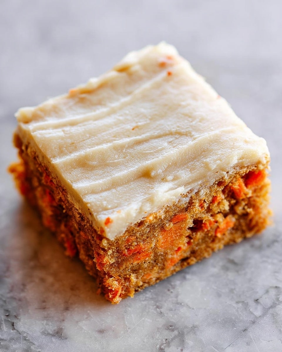A close-up view of a square carrot cake piece showing two layers: the bottom layer is a moist, crumbly cake with visible small orange carrot shreds, and the top layer is a smooth, slightly creamy, light beige frosting with a textured, soft surface with faint lines across it; the cake piece sits alone on a white marbled texture, highlighting the contrast between the warm, earthy colors of the cake and the pale frosting. photo taken with an iphone --ar 4:5 --v 7