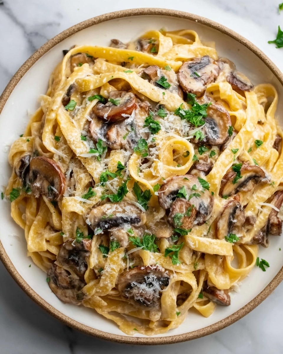 A white plate filled with creamy fettuccine pasta topped with sautéed mushroom slices and sprinkled with grated cheese and chopped parsley. The pasta strands are coated with a smooth, light-colored sauce, intertwined and slightly glossy. The mushrooms are medium brown with a tender texture, scattered evenly over the noodles. The dish rests on a white marbled surface. Photo taken with an iphone --ar 4:5 --v 7