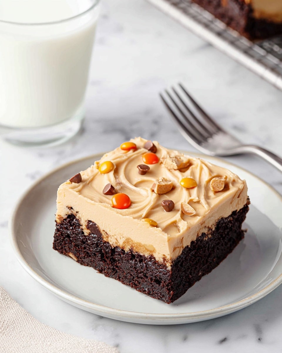 The image shows a thick two-layered dessert on a white plate. The bottom layer is a dark brown, moist-looking chocolate cake with a smooth texture. The top layer is a creamy light tan frosting, spread evenly and garnished with small round orange and brown candy pieces, along with tiny crunchy bits scattered across. A piece of the dessert is cut and placed slightly to the side, revealing the rich texture of the chocolate layer. In the background, there is a tall glass of milk, and a silver spoon rests behind the dessert on a white marbled surface. Photo taken with an iphone --ar 4:5 --v 7