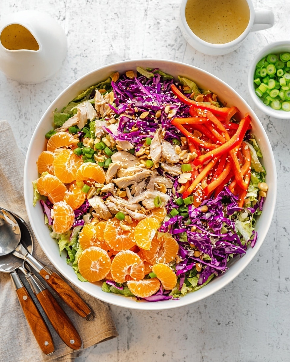A large white bowl filled with a colorful salad arranged in layers: the bottom layer is shredded green leafy lettuce, topped with bright purple shredded cabbage and thin orange carrot strips. On top, there are slices of red bell pepper, small pieces of shredded cooked chicken, and several peeled orange mandarin segments scattered evenly. The salad is sprinkled with whole chopped almonds, toasted sesame seeds, and thinly sliced green onions. The bowl sits on a white marbled surface with a small white jug of dressing above it and a white bowl with more sliced green onions nearby. A pair of shiny silver salad utensils with wooden handles rests on the left. photo taken with an iphone --ar 4:5 --v 7