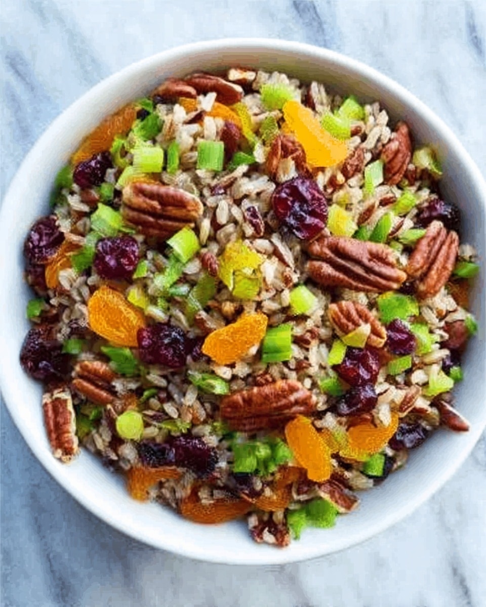 A white bowl filled with a colorful mixed grain salad sits on a white marbled surface. The salad has visible layers of brown and wild rice mixed together, topped with bright orange dried apricot pieces, dark red dried cranberries, light green celery slices, chopped green onions, and scattered pecans. The textures vary from soft and chewy dried fruits to crunchy nuts and fresh vegetables. The overall look is vibrant with a mix of warm and cool colors spread evenly across the bowl. Photo taken with an iphone --ar 4:5 --v 7