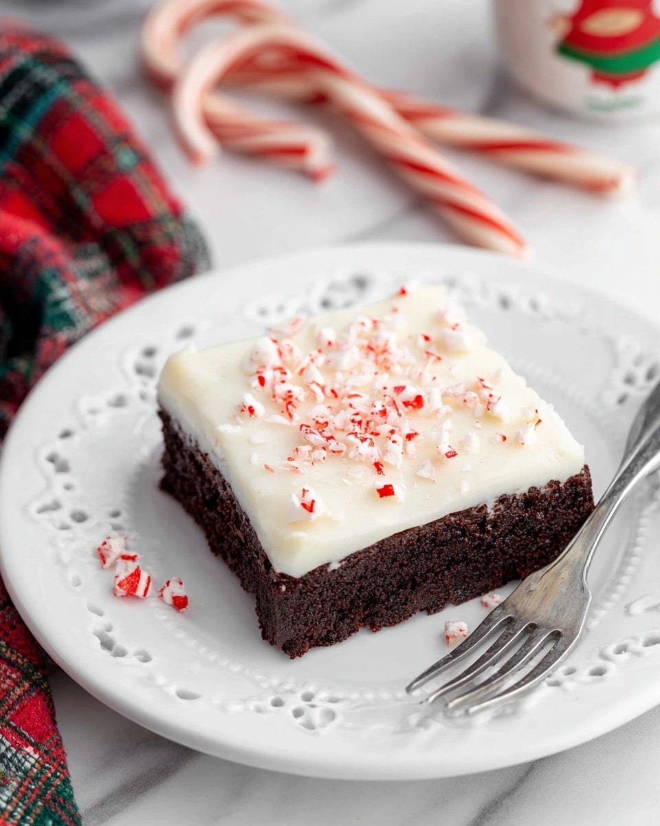 A square piece of dark brown brownie with a thick, smooth white frosting layer on top, sprinkled with small pieces of crushed red and white candy cane. The brownie sits on a white plate with delicate embossed patterns and cut-out details around the edge. Beside the brownie on the plate, there are a few small candy cane pieces. In the background, two whole candy canes lie on a white marbled surface near the plate, with a hint of a red and green plaid cloth and a Santa-themed cup partially visible. A silver fork rests on the plate’s right side. photo taken with an iphone --ar 4:5 --v 7