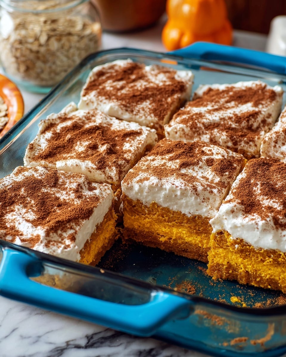 A glass baking dish filled with six square pumpkin cake pieces, each with two visible layers: a bottom soft golden-orange cake layer and a thick white cream layer on top, dusted generously with dark brown cinnamon powder. One piece is partly missing, showing the moist texture of the cake. The dish sits on a white marbled surface with some blurred background items like a jar with cinnamon sticks, oats, and an orange pumpkin. photo taken with an iphone --ar 4:5 --v 7