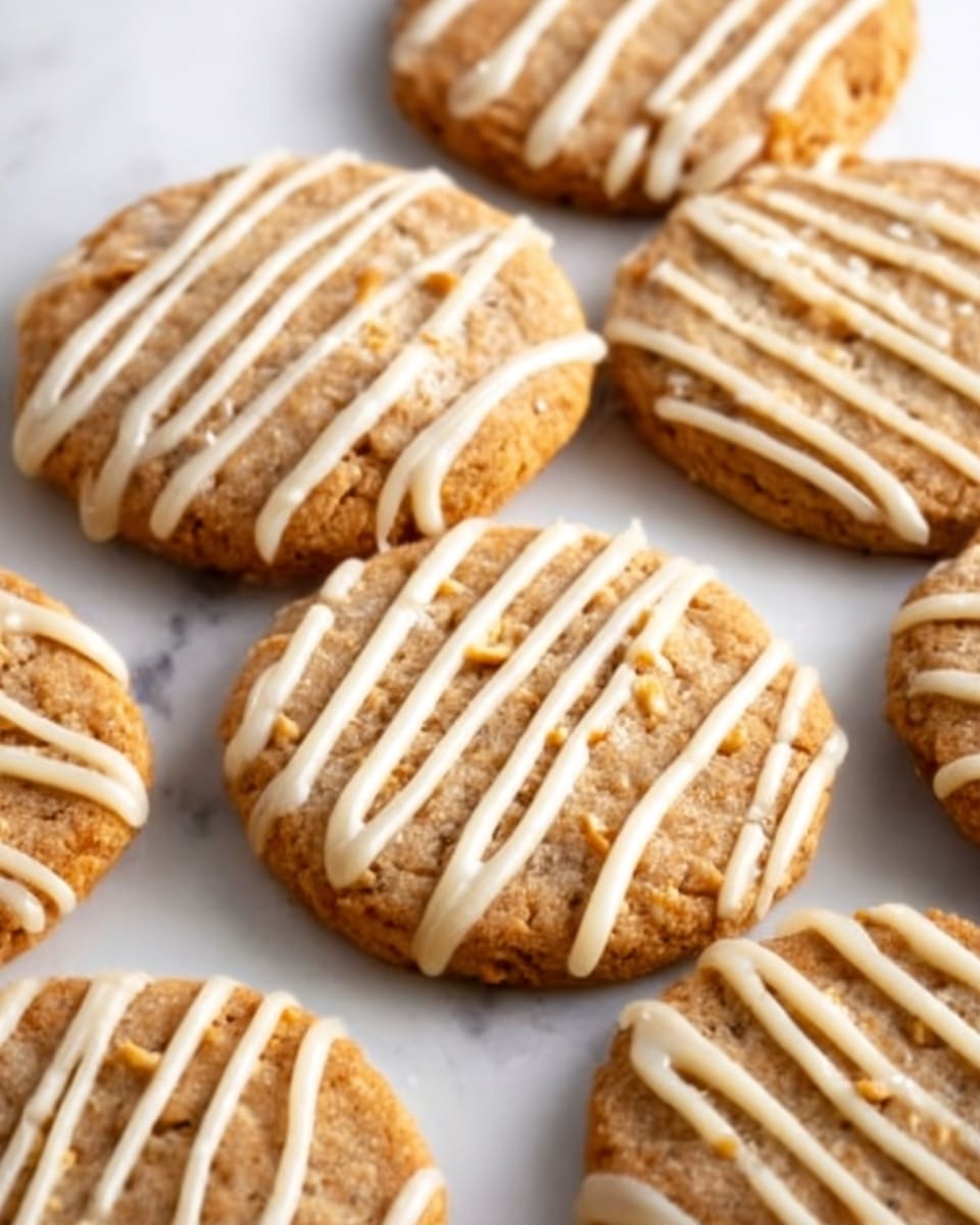 A group of round cookies with a golden-brown color and slightly rough texture are arranged closely on a white marbled surface. Each cookie is topped with thin, uneven white icing lines drizzled across in diagonal patterns, adding a contrasting smooth texture and a light cream color over the warm cookie base. The cookies look soft and crumbly with small visible bits inside, and the light from above highlights their slightly uneven edges and glossy icing. photo taken with an iphone --ar 4:5 --v 7