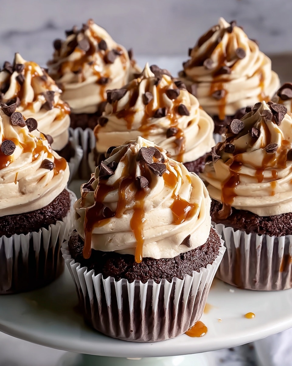 The image shows several chocolate cupcakes with three distinct layers. The base layer is a dark brown chocolate cupcake in a white paper liner with ridges. The middle layer is a swirl of light beige creamy frosting, generously piped in tall, textured peaks with ruffled edges. The top layer is a drizzle of shiny caramel sauce cascading down the frosting, with small dark chocolate chips scattered over it. The cupcakes sit closely together on a white plate, placed on a white marbled surface with some caramel drips around. Photo taken with an iphone --ar 4:5 --v 7