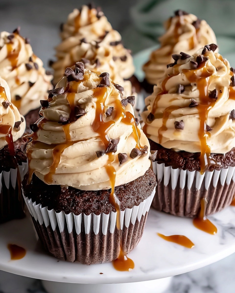 The image shows dark chocolate cupcakes with one main cupcake in front. Each cupcake has two layers: the bottom layer is a dark, rich chocolate cake with a slightly rough texture, and the top layer is a thick swirl of light caramel-colored frosting with a smooth and creamy texture, decorated with small chocolate chips scattered on top. Caramel sauce is drizzled over the frosting, creating shiny golden-brown streams that run down the sides. The cupcakes are in white paper liners and sit on a white plate with a few drops of caramel sauce around. The background is a white marbled texture. photo taken with an iphone --ar 4:5 --v 7