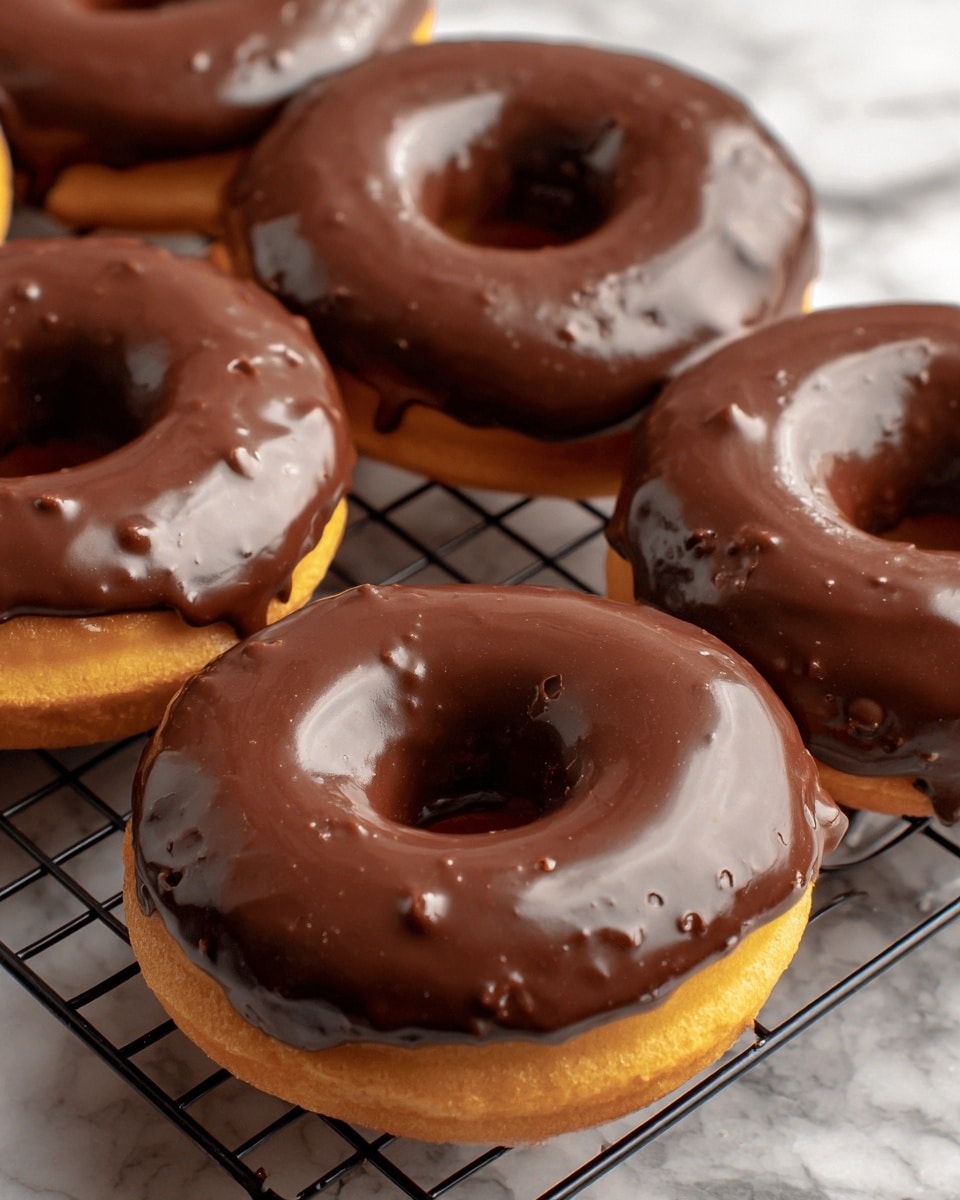 The image shows five donuts with a golden-brown base and thick, shiny chocolate glaze covering the top half of each donut. The glaze looks smooth and slightly glossy, with small textured spots where it thickens. The donuts are arranged on a black cooling rack placed on a white marbled surface. The rich chocolate coating contrasts with the light, soft dough underneath. Photo taken with an iphone --ar 4:5 --v 7