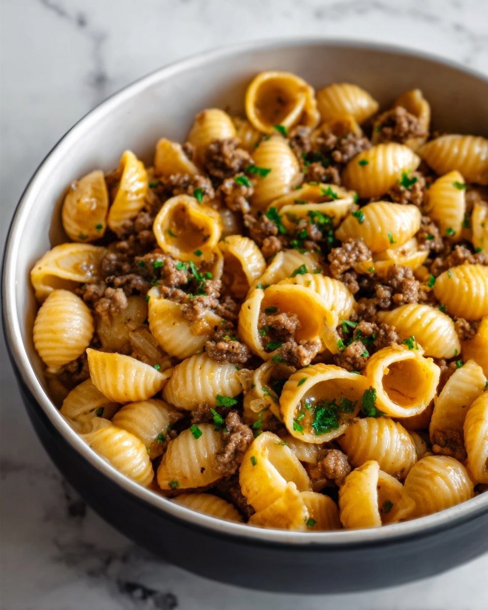 A white bowl filled with shell pasta covered in a thick, brown meat sauce with visible ground beef pieces. The pasta is shiny with a light coating of sauce and sprinkled with finely chopped green herbs on top. The dish looks warm and hearty, with a simple, comforting feel. The bowl sits on a white marbled surface. Photo taken with an iphone --ar 4:5 --v 7