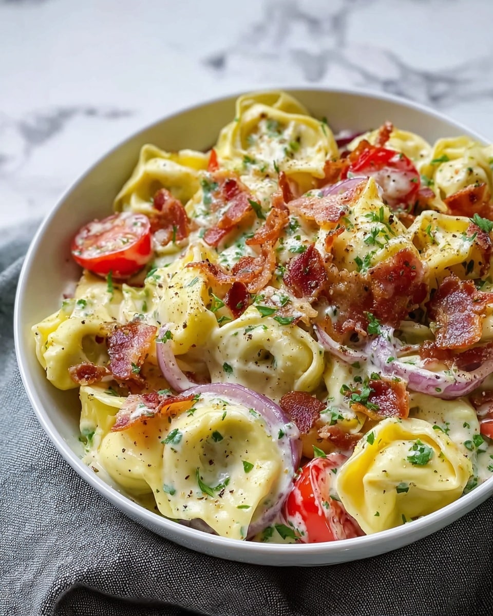 A white bowl filled with creamy pasta tortellini, each piece yellow with a soft, smooth texture, covered in a rich white sauce. Mixed between the pasta are bright red cherry tomato halves, thin slices of crispy brown bacon, and translucent purple onion rings. The dish is sprinkled with fresh green herbs and cracked black pepper, adding specks of color and texture all over. The bowl sits on a surface with a white marbled texture. Photo taken with an iphone --ar 4:5 --v 7