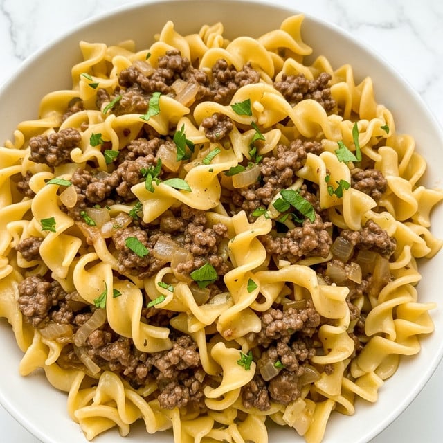 A close-up view of a dish featuring wide, ruffled egg noodles mixed with browned ground beef and small pieces of sautéed onions, all coated in a glossy, brown gravy. The noodles are soft and curly, showing their light yellow color and slightly wavy texture, while the beef is crumbly and dark brown. Small bits of fresh green parsley are scattered evenly on top, adding a pop of color. The mixture looks hearty and rich, filling a white bowl that contrasts with the creamy and meaty layers. The background is a white marbled texture. Photo taken with an iphone --ar 4:5 --v 7