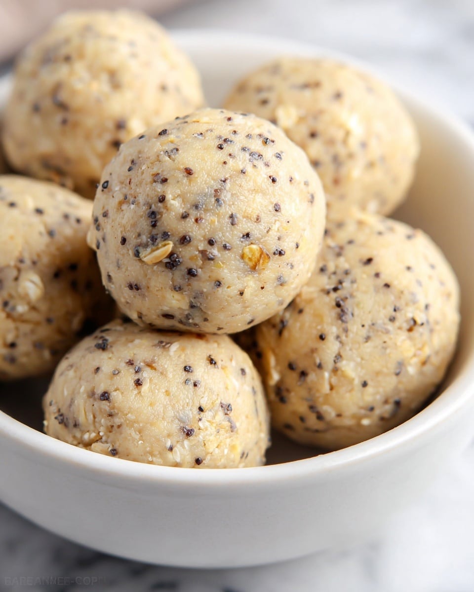 A close-up view of a white bowl filled with small twisted pretzels that are coated in a textured seasoning mix made of green herbs and light-colored garlic bits. The pretzels have a shiny, glazed look with a rough, crumbly layer of seasoning that covers them evenly. The layers show the curved pretzels intertwined inside the bowl, creating a pile with varying shades of golden brown under the green and beige seasoning. The background is softly blurred with a white marbled surface faintly visible. photo taken with an iphone --ar 4:5 --v 7