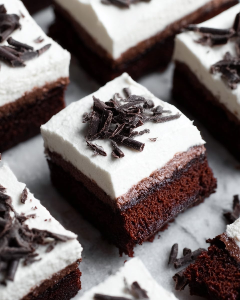 The image shows a close-up of several square chocolate dessert bars arranged together on a white marbled surface. Each bar has two main layers: a thick, dark brown, moist-looking chocolate cake base topped by a thick, smooth white frosting layer. Some bars are slightly cut unevenly, showing soft, dense cake beneath the smooth frosting. Small dark chocolate shavings are scattered on top of the frosting, adding texture and contrast. The lighting highlights the rich textures of the cake and the creamy frosting, making the dessert look fresh and inviting. Photo taken with an iphone --ar 4:5 --v 7