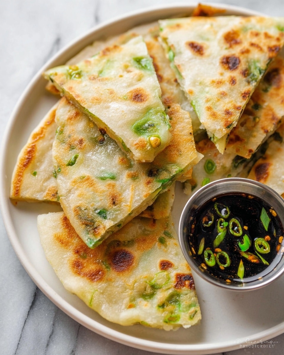 Several triangular pieces of golden-brown scallion pancakes with crispy and slightly charred spots are stacked on a white plate. The pancakes have visible green onion slices embedded in the dough, showing a mix of light tan and green colors with a soft, chewy texture. On the edge of the plate, a small metal cup holds a dark soy-based dipping sauce with green onion pieces floating inside. The whole setup is on a white marbled surface. photo taken with an iphone --ar 4:5 --v 7