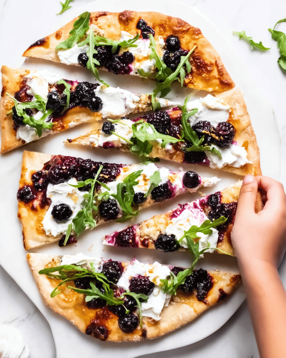 A rectangular flatbread pizza is sliced into four long pieces, placed on a white plate on a white marbled surface. The crust looks thin and golden brown with some crisp edges. The flatbread is topped with dollops of white creamy cheese, dark purple mixed berries evenly spread across, and some fresh green arugula leaves scattered on top. A woman's hand is reaching to pick up one slice from the right side. The colors of the toppings stand out well against the light crust and plate. photo taken with an iphone --ar 4:5 --v 7