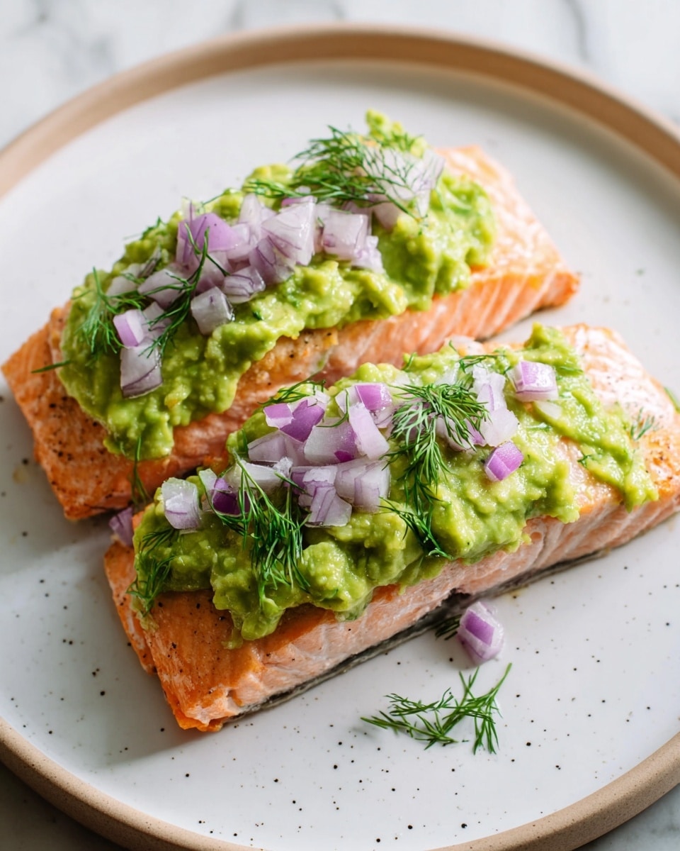 The image shows two pieces of cooked salmon placed side by side on a round white plate with small brown specks. The salmon is pinkish-orange with light white grill marks and flaky texture. On top of the salmon, there is a thick layer of bright green mashed avocado spread evenly but with a rough texture. Small diced pieces of purple and white onion are scattered on the avocado, along with tiny sprigs of fresh green dill. The plate sits on a white marbled surface, and the photo is close-up, showing details of the food's texture and colors clearly. photo taken with an iphone --ar 4:5 --v 7
