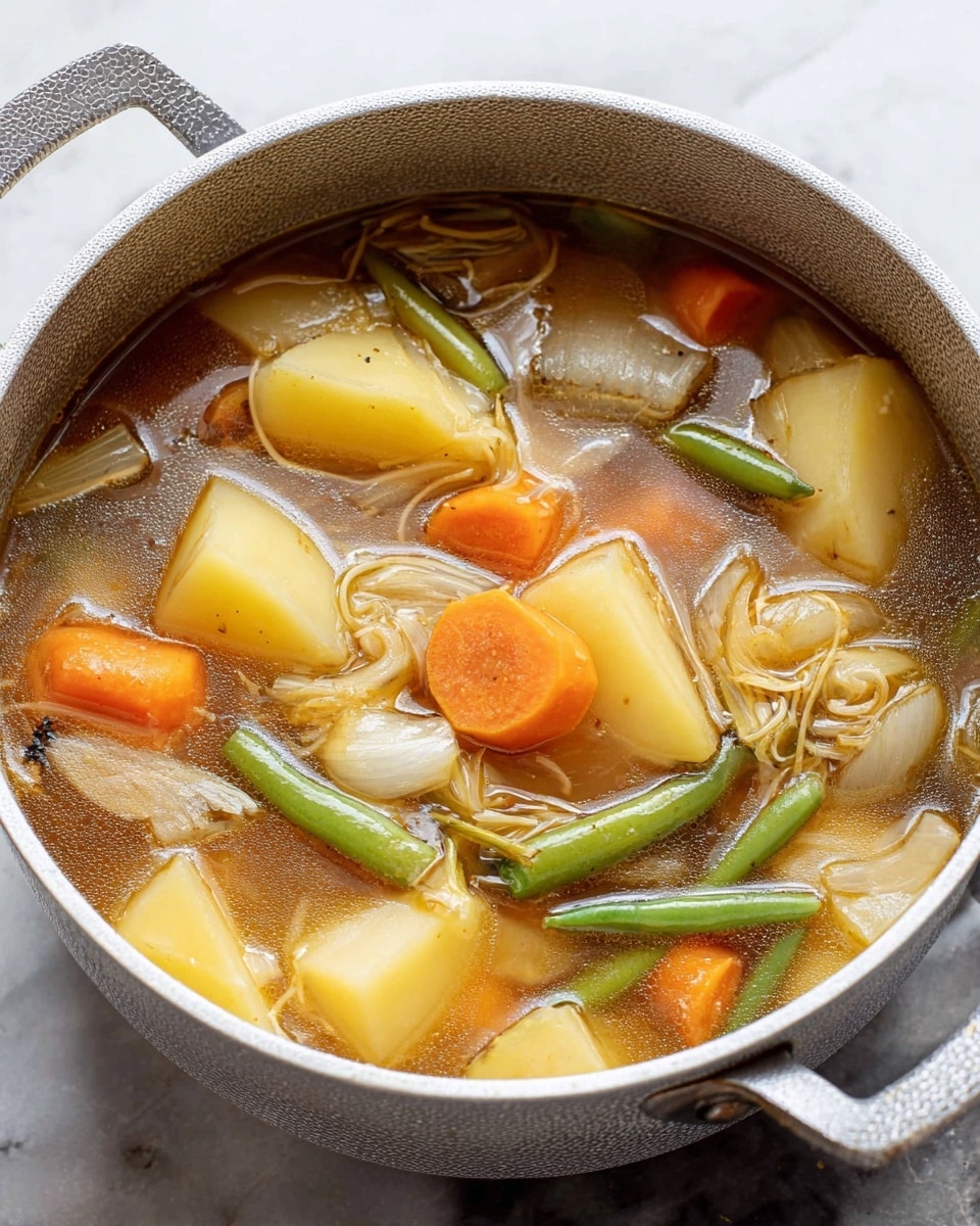A white pot filled with clear brown broth containing large pieces of vegetables and meat. There are thick slices of orange carrot, chunks of yellow potato, sections of green beans cut into thirds, and large wedges of cooked onion floating in the soup. Thin, light-colored noodles are mixed throughout the broth, and a few pieces of cooked brown meat are visible. The pot has a hammered texture and is set on a white marbled surface. photo taken with an iphone --ar 4:5 --v 7