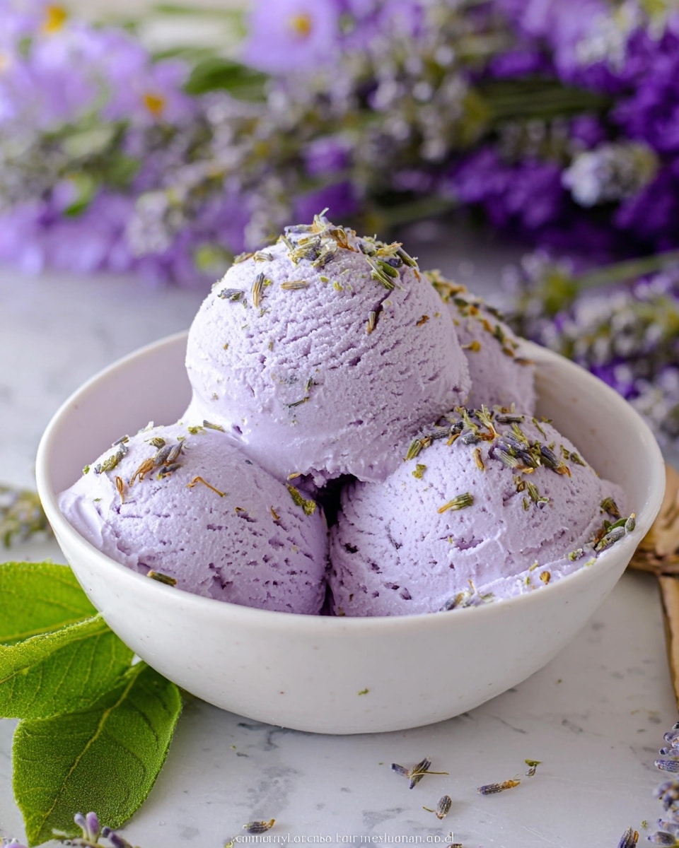 This image shows a white bowl filled with four scoops of light purple ice cream. The scoops are smooth and creamy, stacked closely but not perfectly shaped, creating a rounded mound. The top scoop is sprinkled with small dried lavender buds, adding a greenish-brown texture on the purple surface. In the background, there are blurred sprigs of real lavender flowers with green leaves, all resting on a white marbled surface covered by a floral fabric with small purple and blue flowers. Photo taken with an iphone --ar 4:5 --v 7
