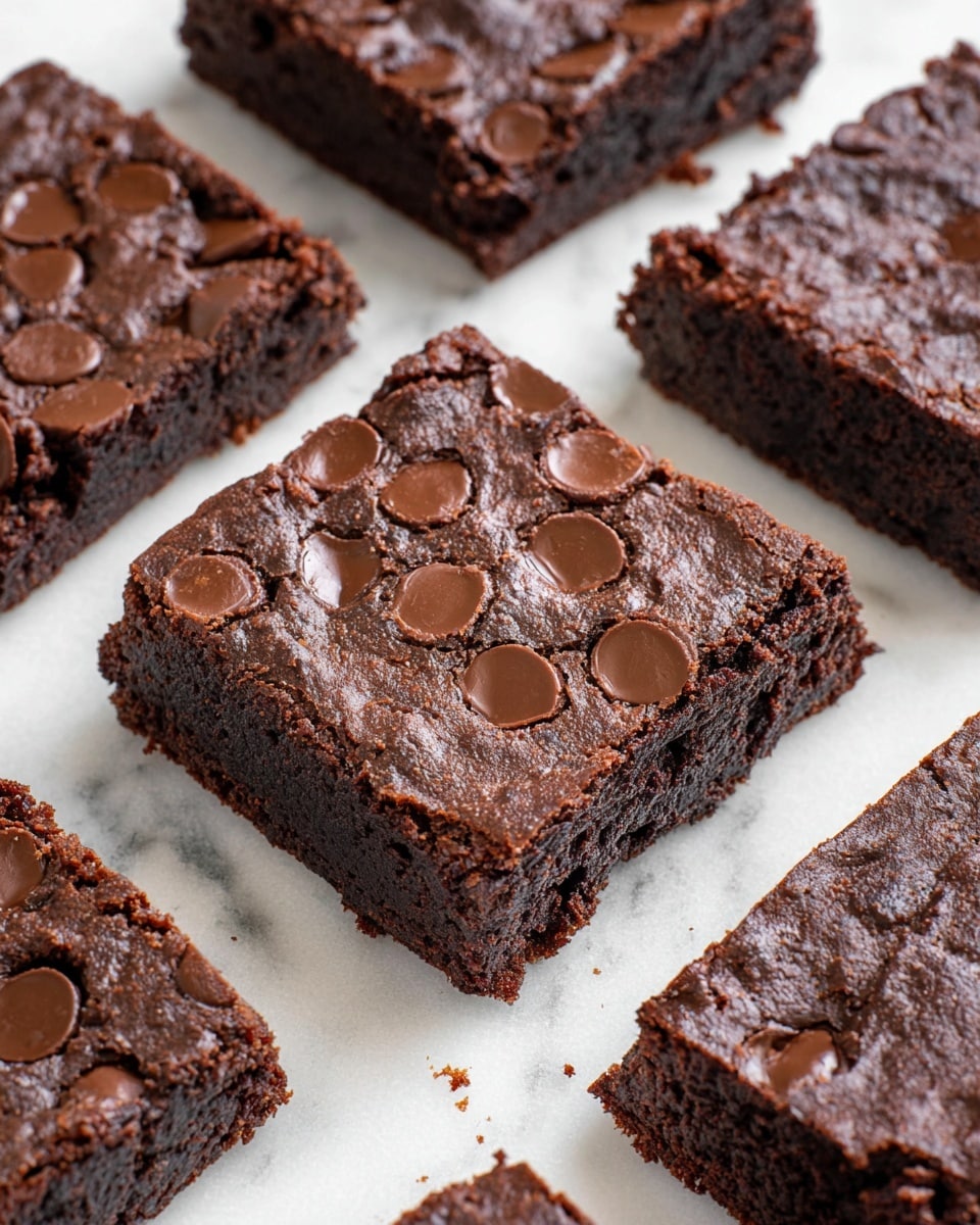 The image shows close-up squares of rich, dark chocolate brownies arranged on a white marbled surface. Each brownie has a thick, dense layer with a moist, fudgy texture that looks soft inside. The top layer is slightly crackled and textured with semi-melted, shiny chocolate chips embedded unevenly across each piece, giving a subtle variation in color and texture. The edges are slightly rough but firm, holding the shape well. The brownies are cut neatly with visible crumbs around the sides. Photo taken with an iphone --ar 4:5 --v 7