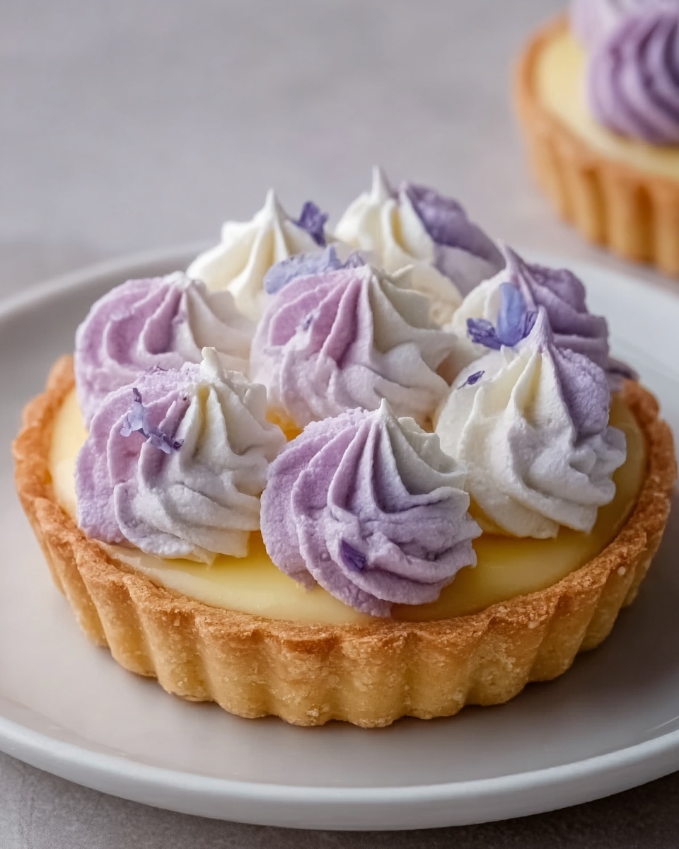 A small tart with a golden, crisp crust forms the base, filled with a smooth, light purple cream. On top, there are dollops of white and pale purple whipped cream, twisted into soft peaks closely packed in a circle, creating a fluffy texture. The tart sits on a white plate, placed on a white marbled surface. The colors focus on soft purples, creamy whites, and warm golden brown from the crust, giving a delicate and fresh look. photo taken with an iphone --ar 4:5 --v 7