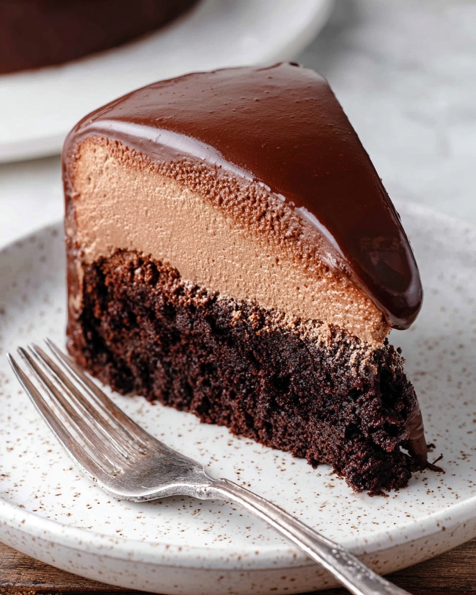 A close-up of a single slice of chocolate cake on a white speckled plate, showing two main layers: a thick, rich dark brown chocolate cake layer on the left with a rough, crumbly texture, and on the right, a smooth, creamy milk chocolate mousse layer topped by a shiny, dark chocolate ganache coating that wraps around the side. A silver fork rests on the plate, with chocolate mousse smeared on its prongs. The plate sits on a white marbled texture surface, with a blurred white plate and cake slice in the background. photo taken with an iphone --ar 4:5 --v 7